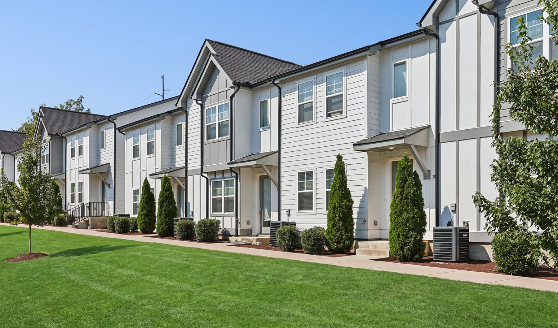 Exterior view of newly constructed two-story townhomes featuring white board and batten siding, dark trim, and landscaped lawn
